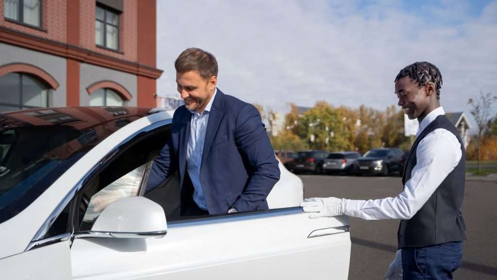 A man in a suit enters a white car as the driver helps open the door for him; Nickelback Tour Brisbane.