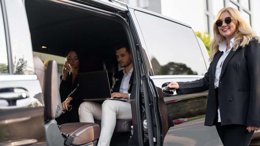 Two passengers working in car with open door.