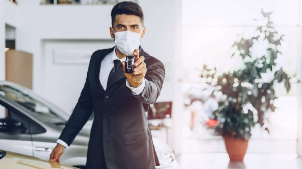 Corporate chauffeur with mask holding car key.