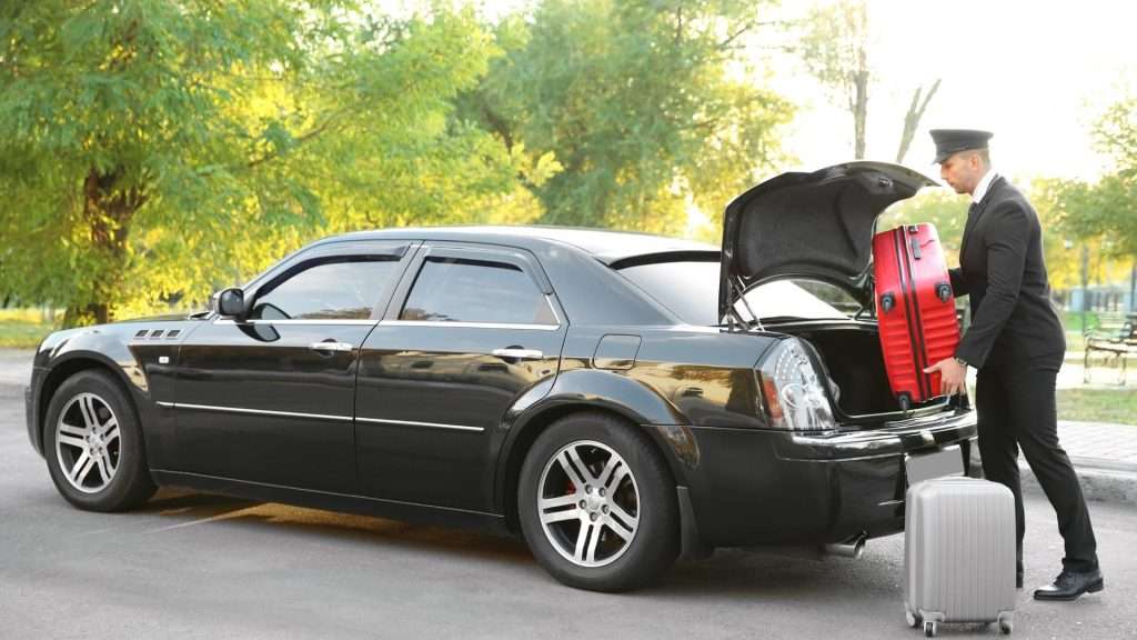 hauffeur assisting with luggage loading into a luxury car trunk