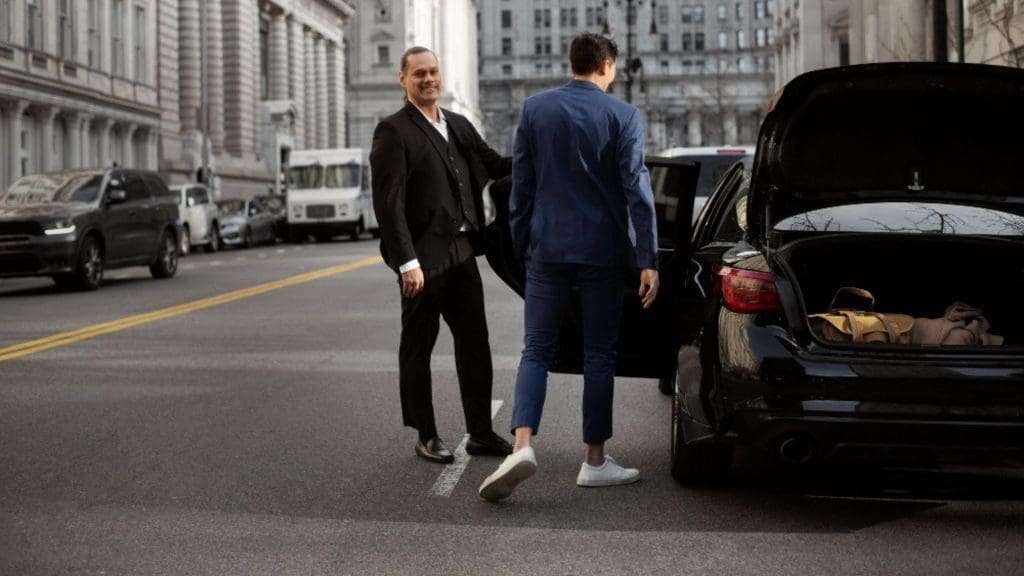 Luxury chauffeur car with suited driver parked in front of corporate building