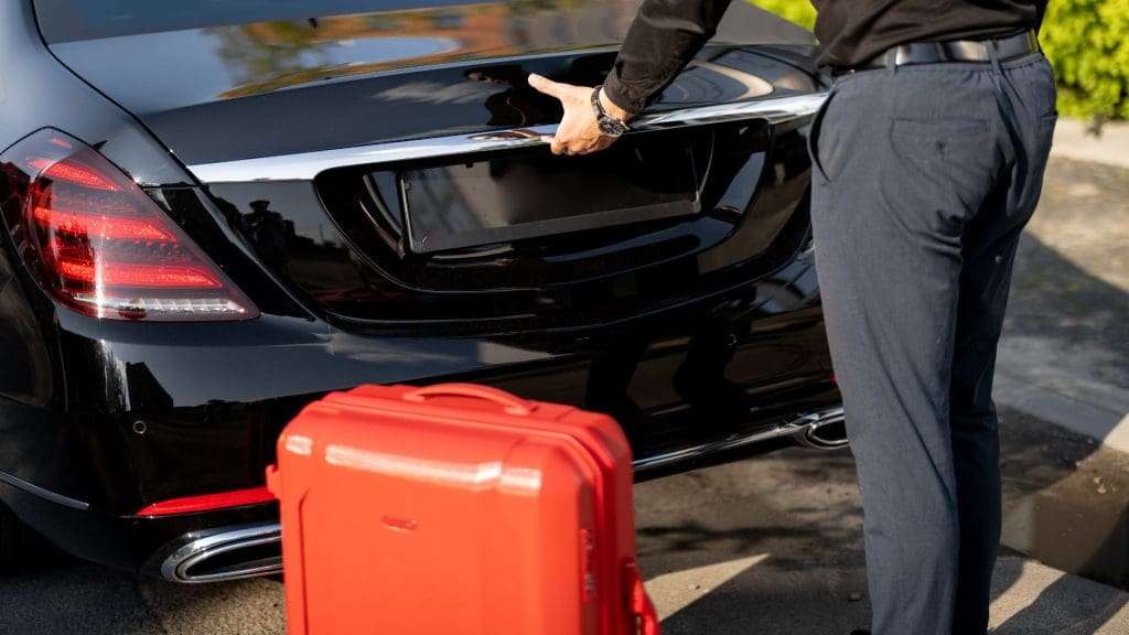 Chauffeurs loading luggage into a parked car trunk.
