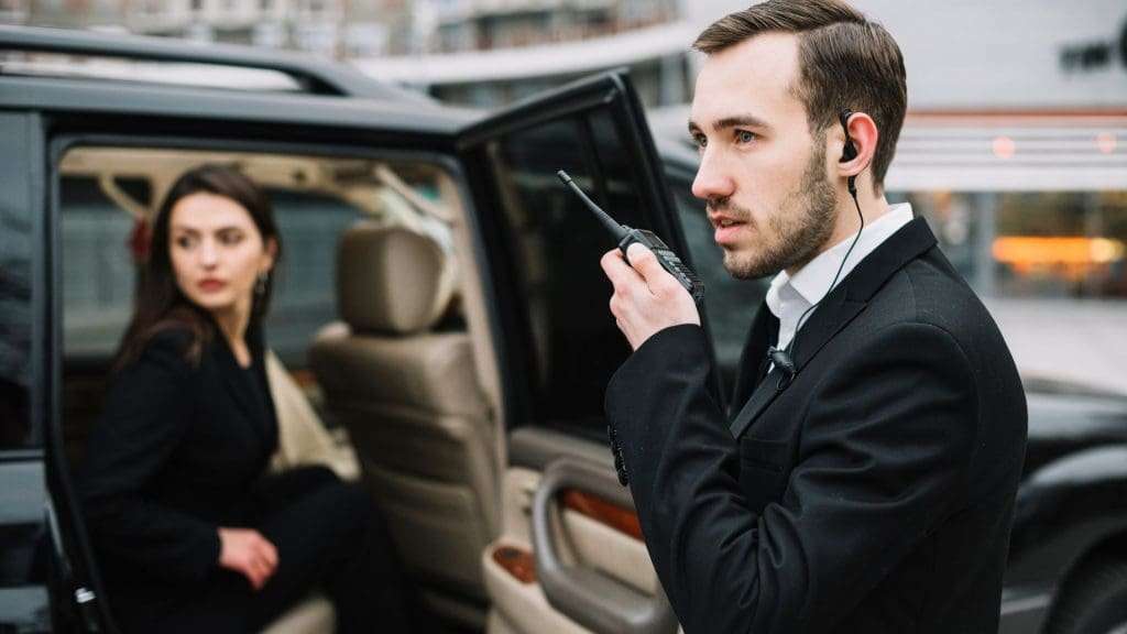 Chauffeur waits in car outside Sydney Airport terminal for passenger pickup.