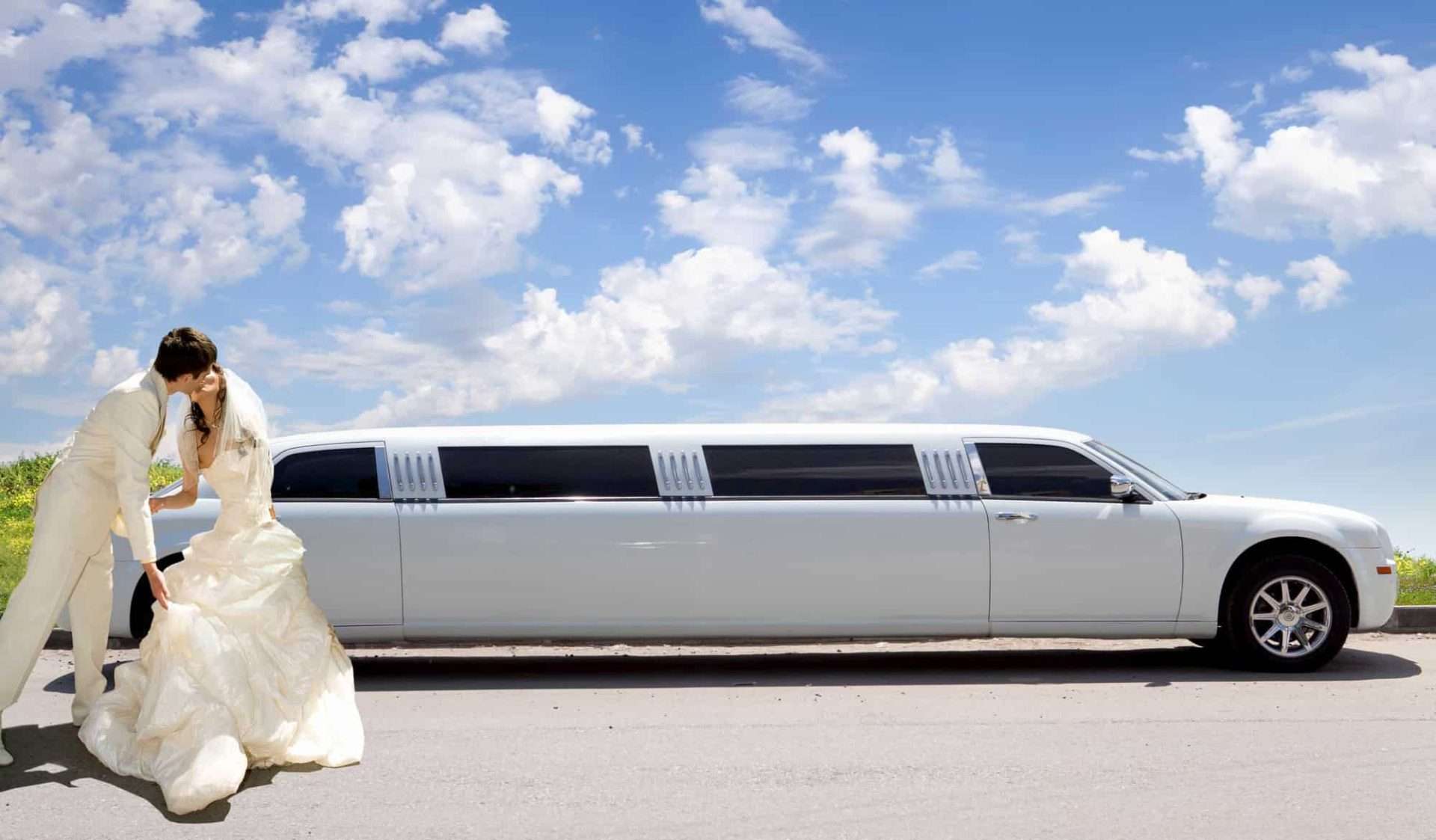 Newlywed couple kissing in front of wedding car