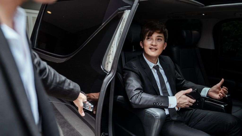 Chauffeurs assist client opening luxury accommodations car door in elegant surroundings