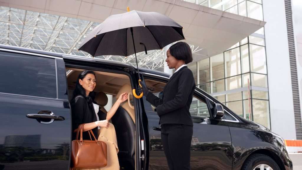 Discover Adelaide: Female chauffeur assists client with umbrella stepping out from car in sunlight