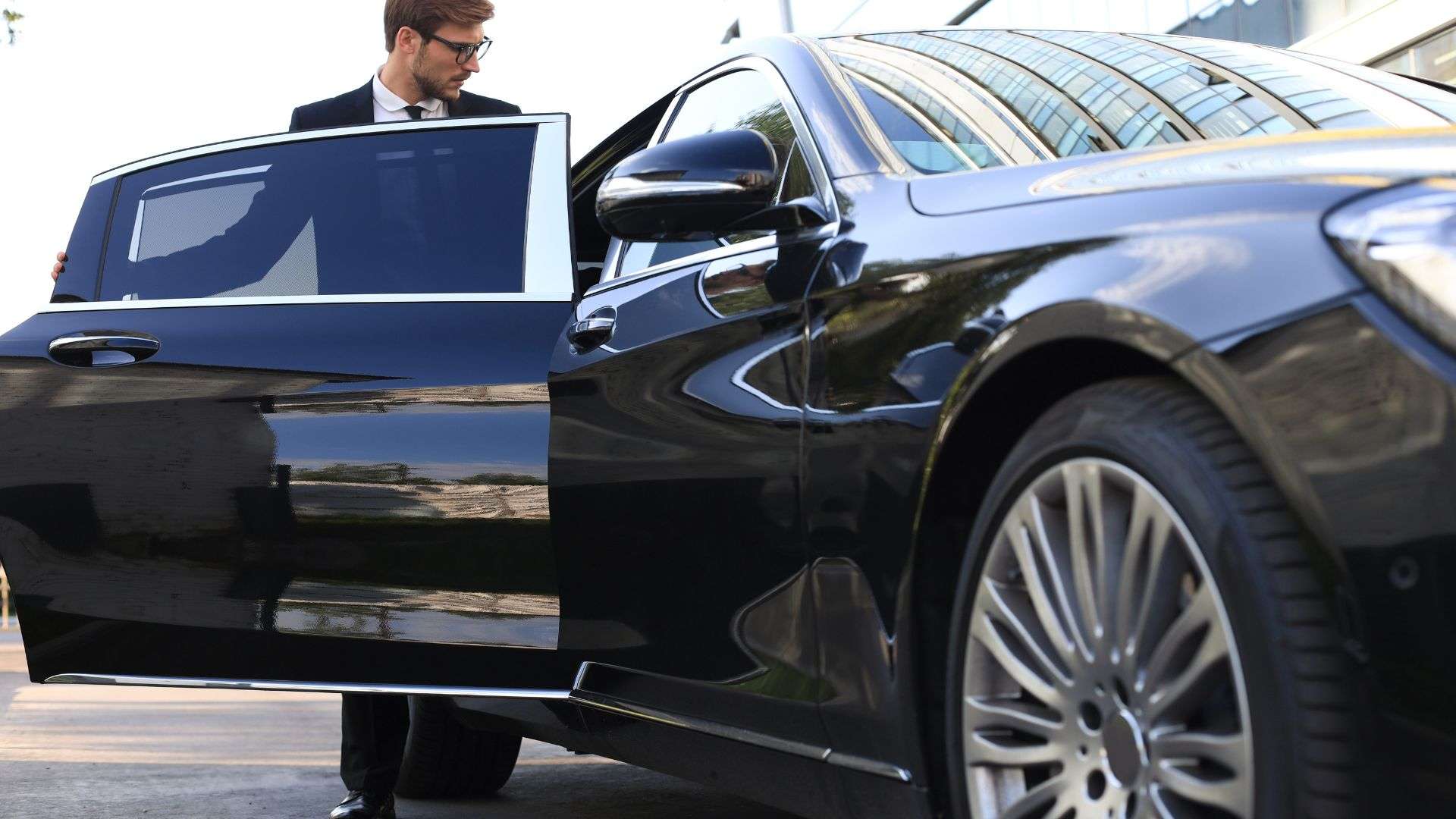 Chauffeur Car in Brisbane luxury black sedan with suited driver holding door open near modern office building in daylight